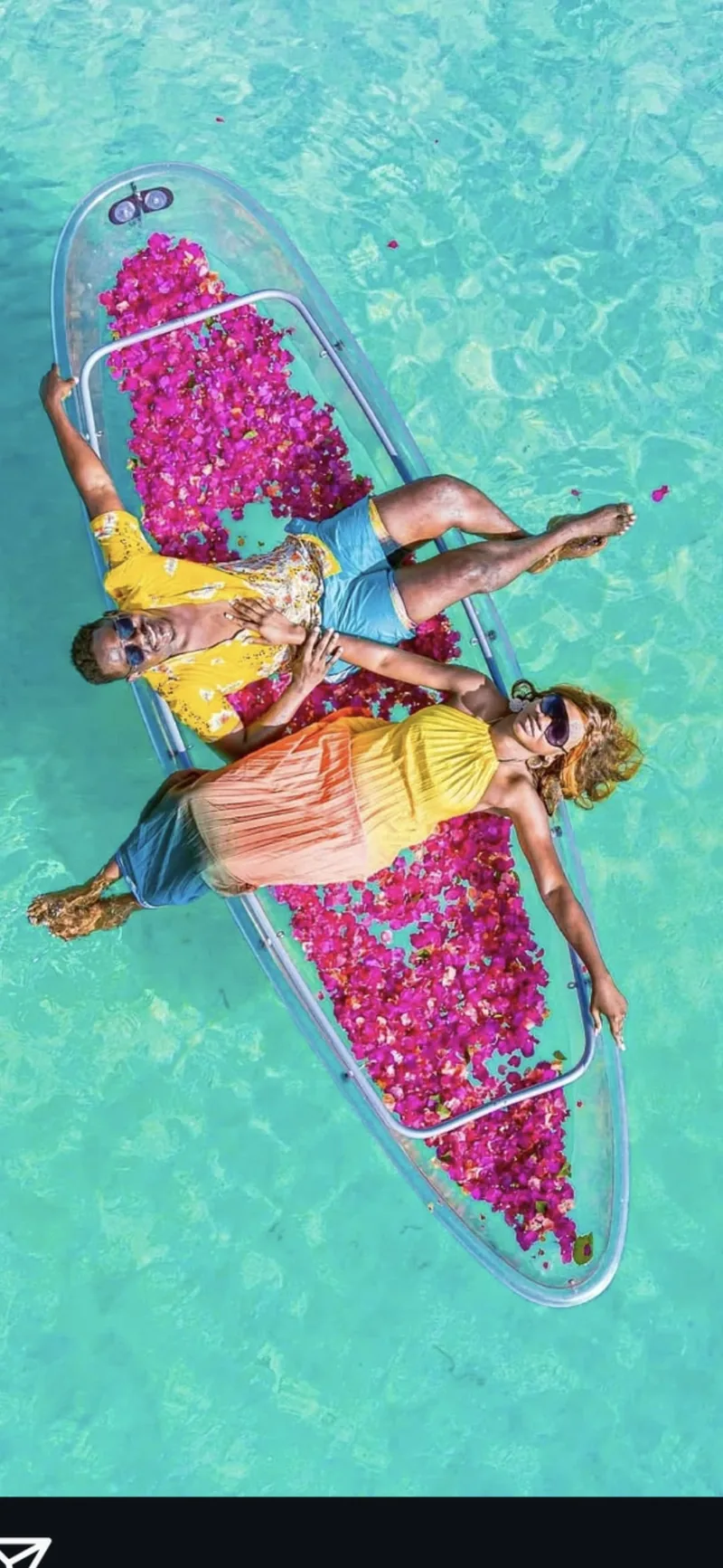 A couple floating among flower petals in a glass-bottom kayak off Zanzibar