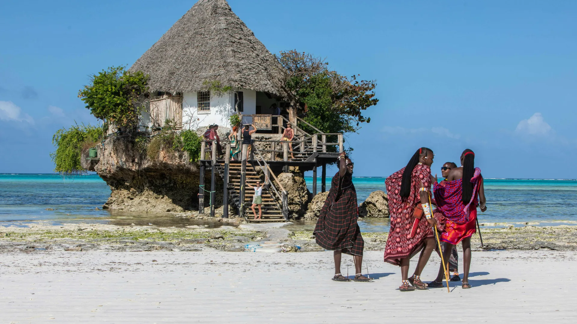 The Rock restaurant standing offshore on the Zanzibar coast, with local guides on the sand